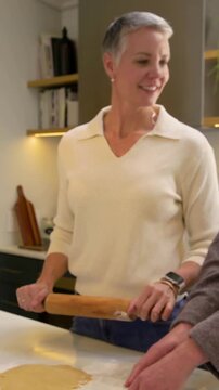 Vertical video: Grabbing rolling pin, cream-sweatered woman rolling dough at kitchen island to bake