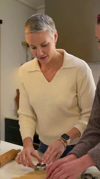 Vertical video: Pin pausing, mature woman pressing cutters into dough at kitchen island for cookies