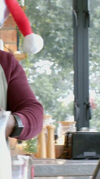 Vertical video: Whisking man in Santa hat and apron following tablet recipe on counter, with whisk