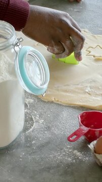 Vertical video: Hand entering pressing cutter in dough for cookies on table burgundy top
