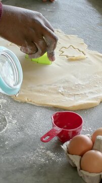 Vertical video: Reaching maroon arm pressing green cutter into dough, making tree cookies with eggs