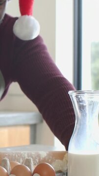 Vertical video: Flour jar open, baker in Santa hat rolling dough in kitchen using pin for cookies