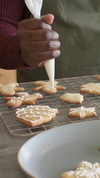 Vertical video: Holding icing bag, cook icing cookies on cooling rack at home in olive-green apron