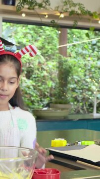 Vertical video: Stirring child with candy cane band mixing in kitchen, adult arriving guiding whisk