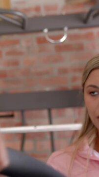 Vertical video: Gripping handle, muscular man pulling cable at garage gym in gray tank, copy space