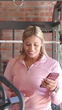 Vertical video: Trainer in gray tank coaching and pedaling bike in home gym, woman scrolling phone