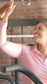 Vertical video: Trainer reaching in, woman in pink top high-fiving and checking phone near machine