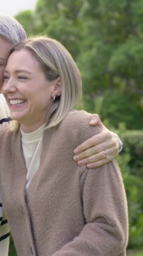 Vertical video: Approaching left, senior hugging daughter in park, supporting, cardigan, copy space