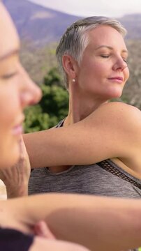 Vertical video: Smiling mature woman doing shoulder stretch on patio to relax, smartwatch, tank top