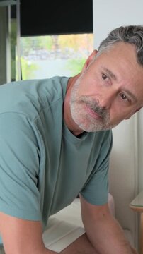Vertical video: Straightening man from edge of bed, turning left toward bathtub to stand, with lamp