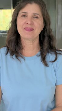 Vertical video: Smiling woman in blue tee camera rolling, leaning on bed and speaking, showing ring