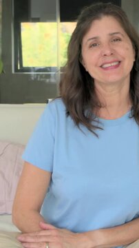 Vertical video: Camera zooming in, woman smiling then laughing on couch with plant, window, ring