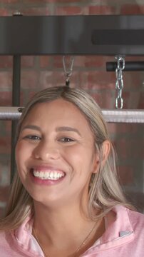 Vertical video: Smiling woman reacting to camera, turning, laughing in gym with chains in pink top
