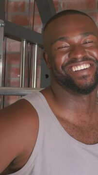 Vertical video: Laughing man in grey tank reacting to off-camera voice at gym machine, copy space