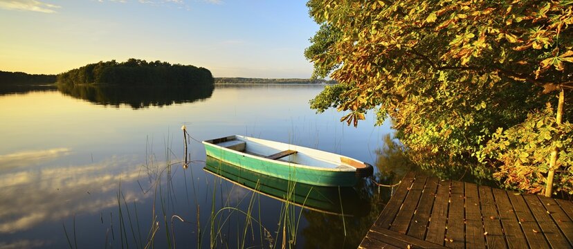 Quiet lake with jetty and rowing boat in the evening in autumn, horse chestnut with autumn leaves on the shore, reeds in the water, Gro&szlig;er Lychensee, Lychen, Uckermark, Brandenburg, Germany