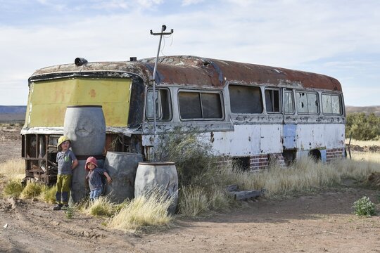 Boy and girl play at car wreck of an old bus, Bosques Petrificados de Jaramillo National Park, Patagonia, Argentina