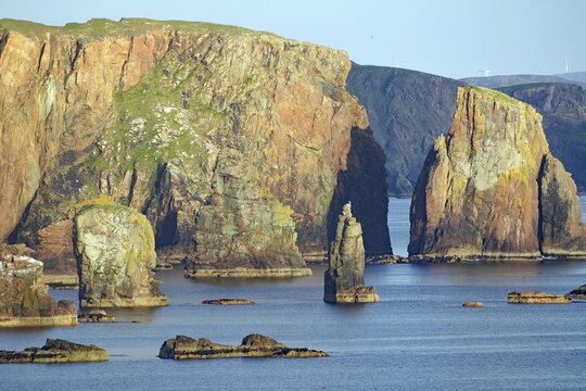Coastal landscape with majestic cliffs in the sunlight by the blue sea, Dore Holm, Hillswick, Eshaness, Shetland Islands, Scotland, United Kingdom
