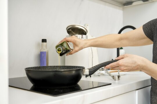 A person is pouring olive oil into a frying pan placed on an electric stovetop in a kitchen