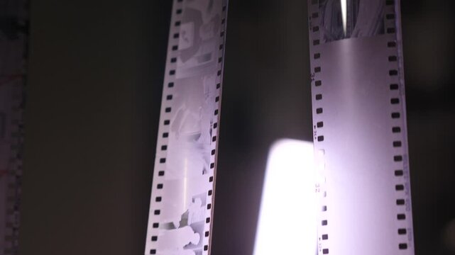 Photographic 35mm film negatives hanging in a darkroom or light table, showcasing the intricate details of vintage photography and the processing of past moments