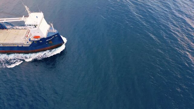 Close-up aerial perspective of a cargo ship bow sailing forward. Focus on the water movement and the ship's front structure.