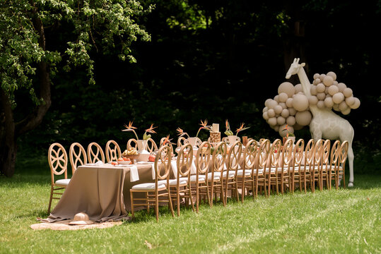 Elegant safari inspired outdoor banquet table with giraffe balloon installation tropical flowers and luxury neutral wedding decor in sunny garden landscape