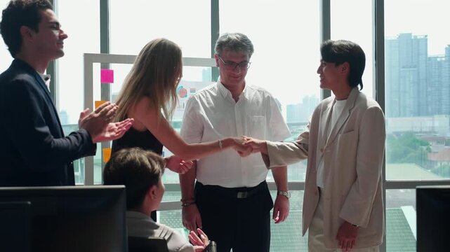 Professional businessman shaking hands with asian businesswoman during office meeting, man and partnership colleagues sitting at computer desk clapping hands with celebrating success business deal.