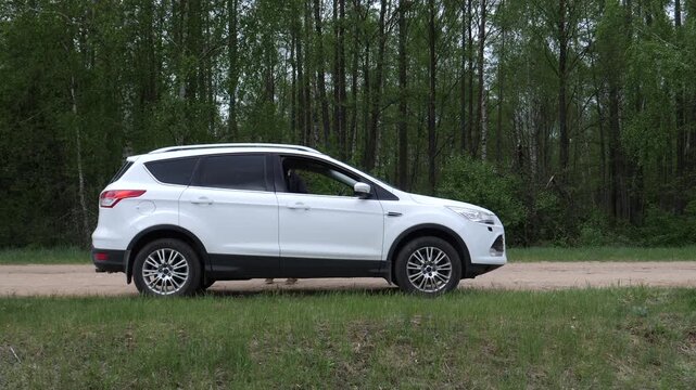 White crossover utility vehicle travelling a dirt road on the edge of a green forest, representing themes of travel, adventure, and nature exploration