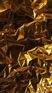 Gold foil surface with crinkled metallic texture reflecting high contrast studio light.