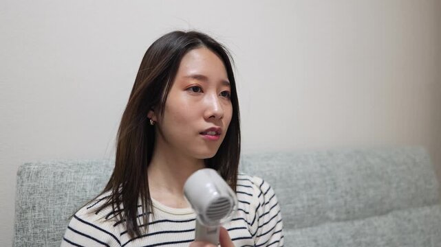 家の中でハンディファンを使って涼む女性のズームイン