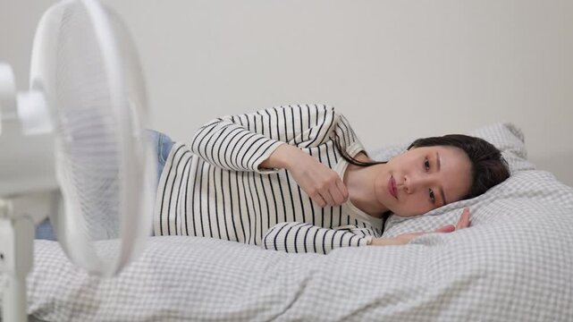 家の中でベッドに横たわって扇風機の風にあたる女性