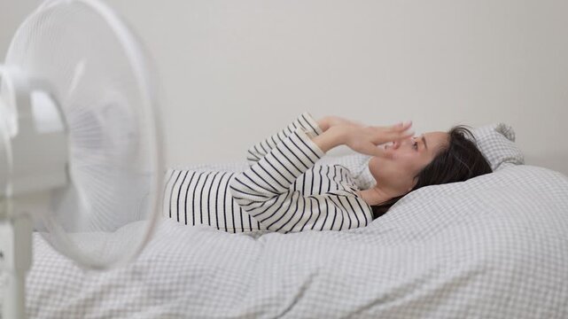 家の中でベッドに横たわって扇風機の風にあたる女性