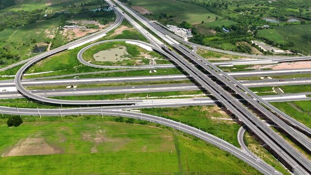 Aerial view of modern highway interchange with multilayer roads and curved ramps surrounded by green farmland, showcasing transportation infrastructure, urban development, and road network planning.
