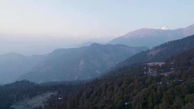 Aerial view of Chopta Tungnath with misty mountain ridges and dense evergreen forests under a soft morning sky in Chopta, Uttarakhand, India.