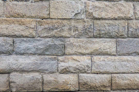 Close up view of weathered vertical stone masonry wall showing horizontal rows of large rectangular granite blocks