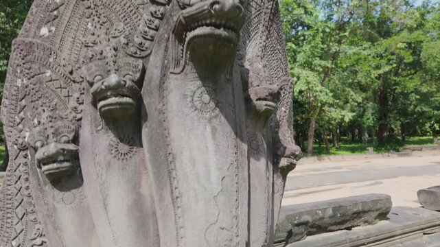 A stone carving of a multi-headed Naga serpent guards the entrance to an ancient temple of Prasat Beng Mealea in Siem Reap, Cambodia. The intricate details showcase traditional Khmer artistry.