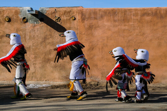 Eagle dancers walking beside an adobe wall