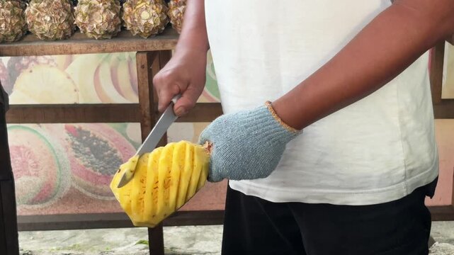 Fruit seller carving fresh pineapple spiral pattern with knife at tropical street fruit stand