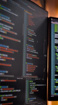 Vertical video close up computer monitors displaying fictional programming code and software development interface, technology workspace concept