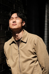 Fototapeta premium Young asian man closing eyes enjoying sunlight