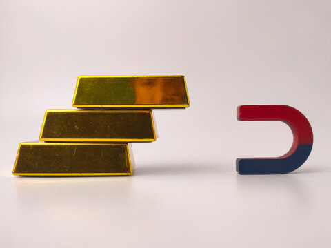 Three replica gold bars stacked in a pyramid structure next to a red and blue horseshoe magnet