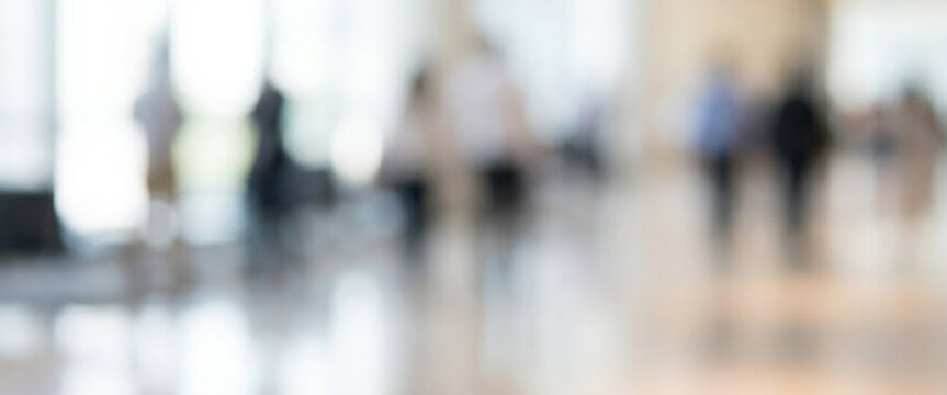 An abstract, blurred image depicting a busy indoor environment filled with indistinct silhouettes of people, creating a sense of motion and activity.