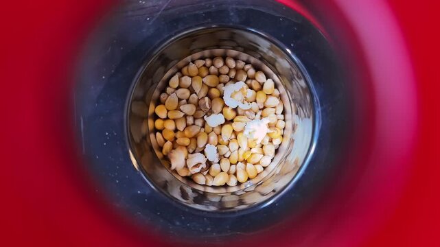 A close-up top down view into a red popcorn machine showing corn kernels starting to pop. High-quality lifestyle footage for cinema, snacks, or home movie night social content.