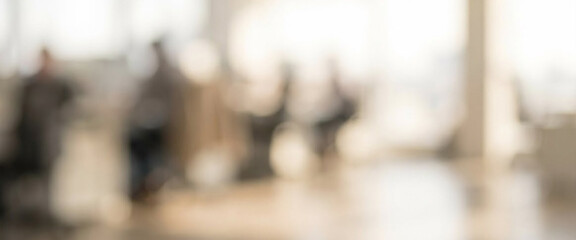 Obraz premium A blurred office environment featuring people engaged in various activities, illustrating a busy and dynamic workspace filled with natural light.