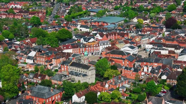 Wide aerial drone footage of Romsey town centre in Hampshire, showing historic buildings, rooftops, streets, shops, roads, trees, residential areas, and the wider town layout on a sunny day.