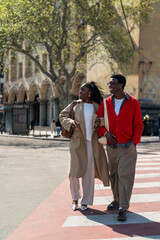 Happy african american students friends man and woman walking smiling through city road together on...