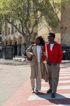 Happy african american students friends man and woman walking smiling through city road together on sunny day, positive black male and female couple exploring town, enjoying conversation and weather.