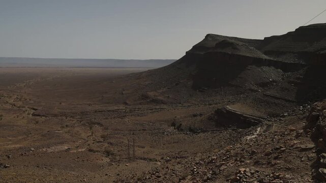 Dark rocky mesa formation towering over endless flat arid desert plain stretching to horizon in Morocco