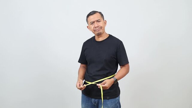 Standing side view of a man measuring his waist or measuring his stomach circumference with a measuring tape, disappointed expression, concept of failed diet or obesity