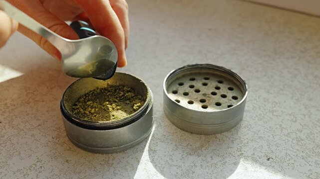 Close-up of hand placing ground herbs into small metal pipe in warm sunlight