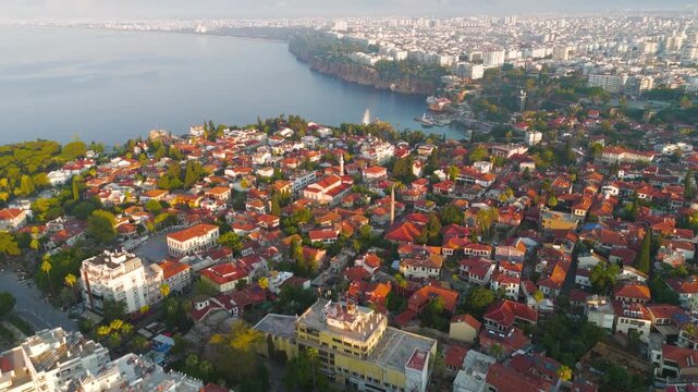 Antalya, Turkey. Kaleici Old Town, dense red-tiled Ottoman houses cascading toward the historic yacht marina, aerial panoramic view with Taurus Mountains rising in morning light. Aerial View, Departu